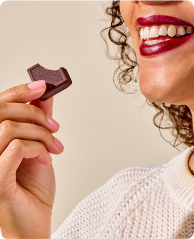 Person smiling while holding a bitten piece of chocolate.